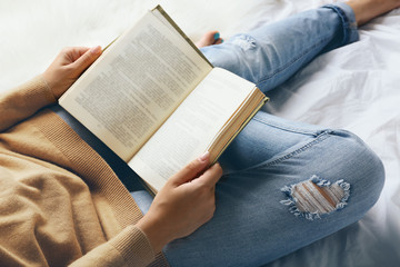 Woman in blue jeans reading book on bed top view point