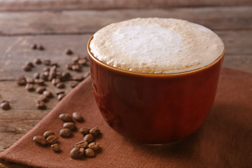 Cup of coffee on napkin and coffee beans on wooden background