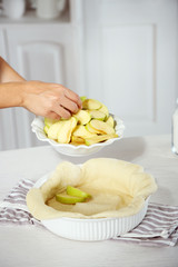 Woman making apple pie on wooden table, on light background