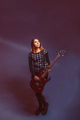 European-looking girl in a sweater holding a guitar and looking 