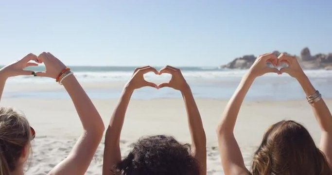 Group of friends making heart shape gesture with their hands on the beach