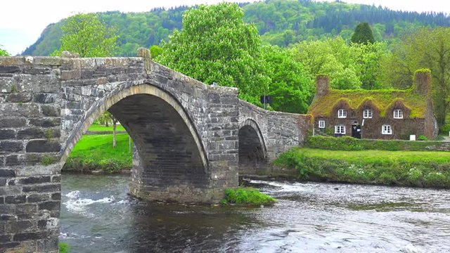 A beautiful bridge over a river with a moss covered house in the distance, Wales.
