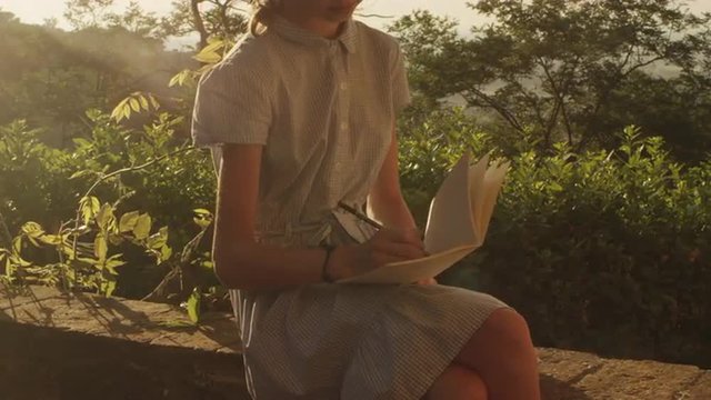 Girl is Drawing in a Notebook at Sunset Time