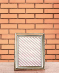 Fototapeta premium Old frame standing on table on brick wall background
