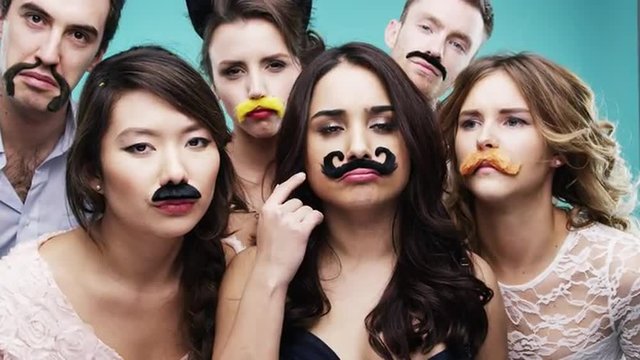 Multi racial group of people wearing false mustache for movember slow motion party photo booth 