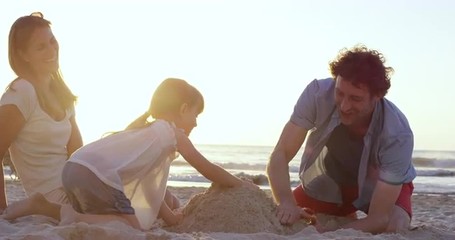 Happy family playing on the beach building sand castle at sunset - Powered by Adobe