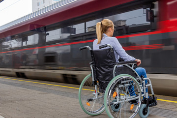 Frau sitzt in einem Rollstuhl auf einem Bahnhof