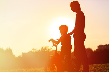 father and son having fun riding bike at sunset