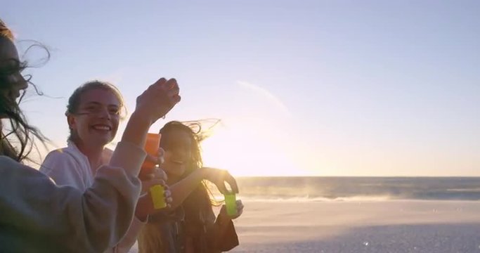 Girl friends blowing bubbles on beach at sunset slow motion