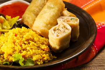 Portion baked spring rolls with vegetables and rice on a plate.