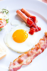 fried eggs with bacon, sausages and toasts on white plate