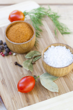 Spices: salt and pepper in wooden pot with tomatoes and herbs close-up, selective focus