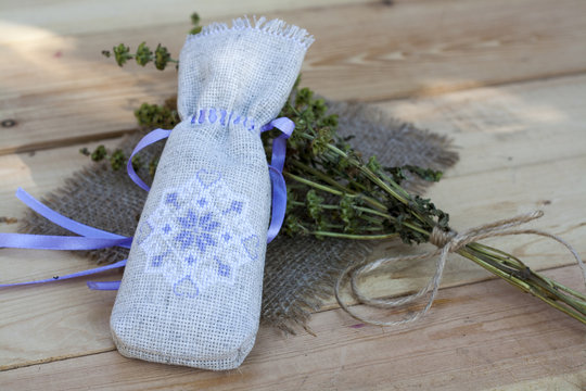 Sachet with ukrainian embroidery, sheaf of wheat and dried herbs on wooden background
