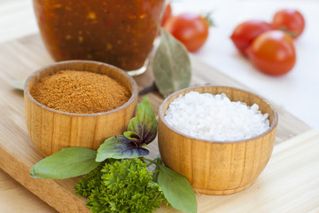 Spices: salt and pepper in wooden pot with tomatoes and herbs close-up, selective focus