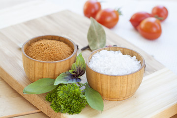 Spices: salt and pepper in wooden pot with tomatoes and herbs close-up, selective focus