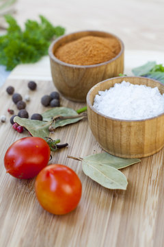 Spices: salt and pepper in wooden pot with tomatoes and herbs close-up, selective focus