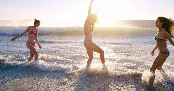 Young women splashing in waves in slow motion playing in ocean on tropical beach