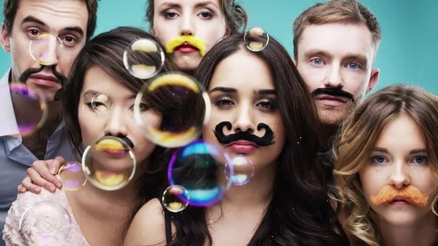 Multi racial group of people wearing false mustache for movember slow motion party photo booth 