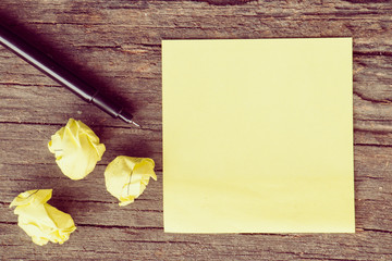 Yellow crumpled papers put on wooden with note and pen, vintage tone style.