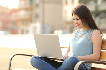 Student girl browsing a laptop sitting in a bench