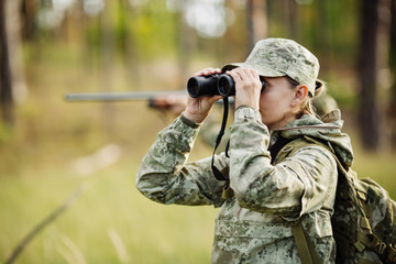 Hunter with shotgun regardant à travers des jumelles en forêt