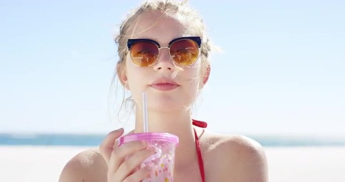 Close up portrait of beautiful young teenage girl drinking water from pink plastic cup on tropical beach slow motion