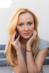 Sensual blonde woman sitting on wooden bench. She is using mobile phone.