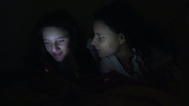 4K surprised teens friends surf internet on smartphne, tablet hidden under bed blanket look pictures on social network. UHD stock video