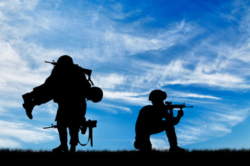  Silhouette of a soldier carries a wounded soldier - obrazy, fototapety, plakaty