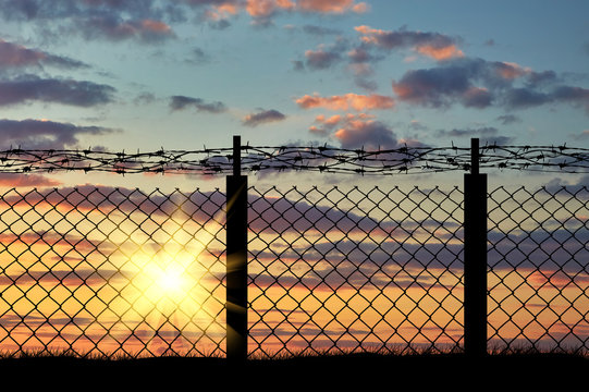 Silhouette of iron fence with barbed wire on the background of sunset