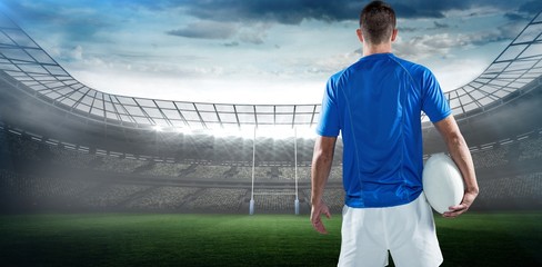Composite image of rear view of rugby player holding ball aside