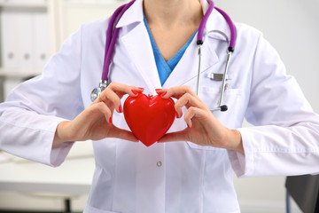 Young woman doctor holding a red heart, in office