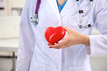 Young woman doctor holding a red heart, in office