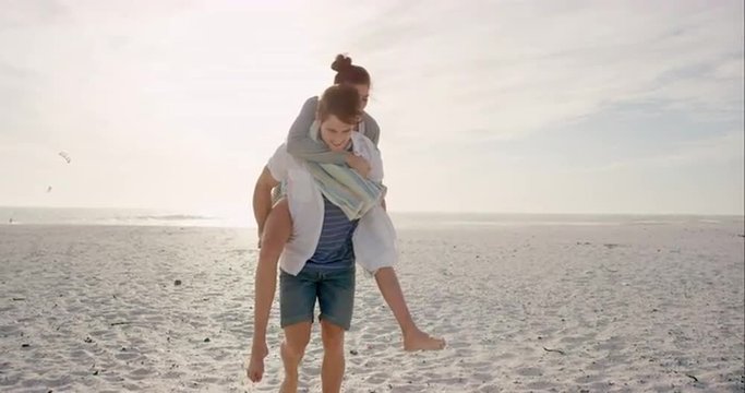 Young couple holding hands walking towards sunset on empty beach