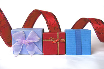 Three gift boxes, red, blue and violet, with decorative tape behind, isolated on white background.