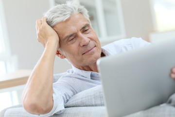 Senior man relaxing in sofa and using digital tablet