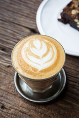 A cup of Latte art coffee on wooden table with brownies cake on