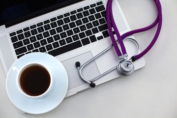 A medical stethoscope near a laptop on a wooden table, on white