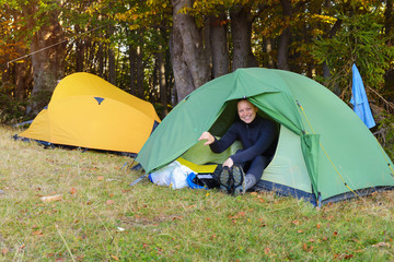 Laughing hiker woman is resting in tent in autumn mountains.