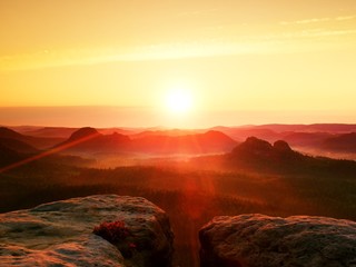 Warm misty autumn land in red colorful shadows. Rocky gulch full of purple fog and Sun is hidden in...