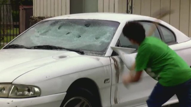 A man destroys his car with a sledgehammer.