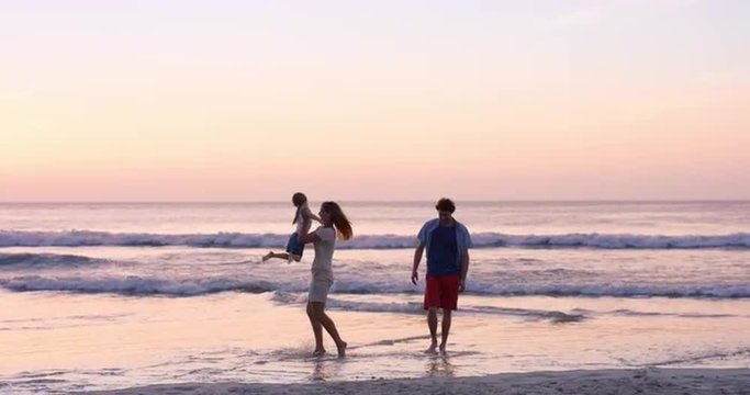 Mother swinging little girl around Happy family on the beach holding hands  at sunset on vacation