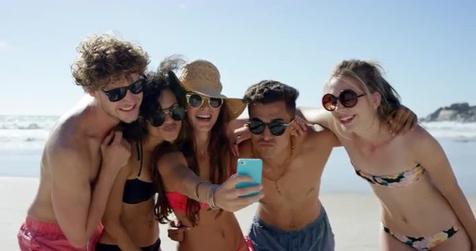 Mixed race group of friends taking selfies on the beach using phone camera