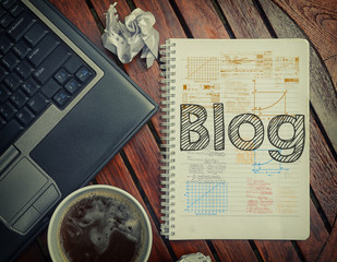 Notebook with text inside Blog on table with coffee, laptop pc a