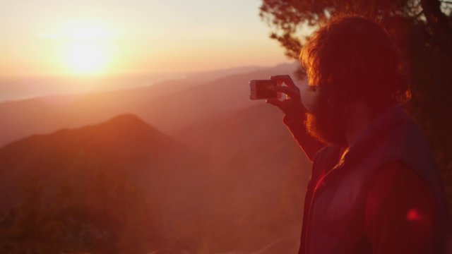 A man takes a picture of the sunset at a campsite.