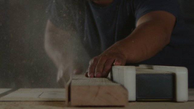 A woodworker saws a plank on a workbench.