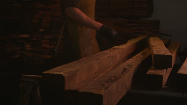 A woodworker selects and carries away a board from a stack of planks in a woodworking shop.