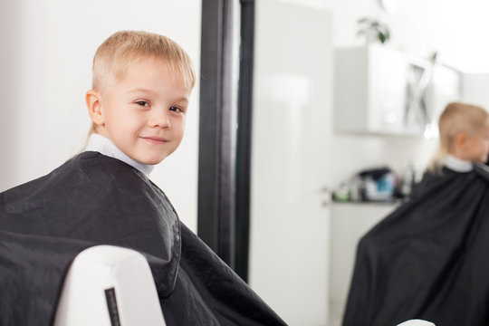 Cheerful male child is getting a hairstyle in hairdressers