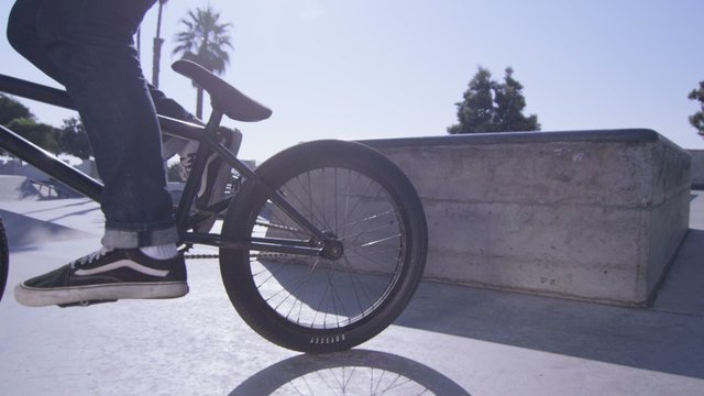 A BMX bike rider peddles out of frame at a skatepark.