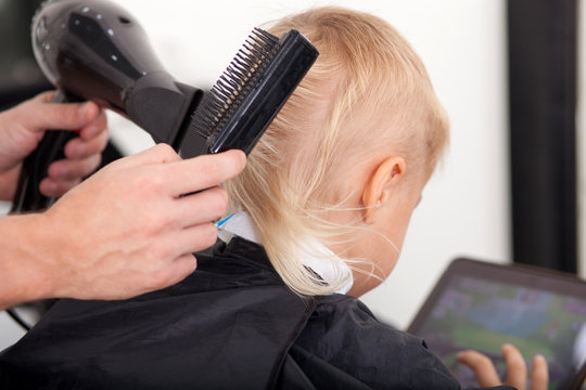 Skilled young hairdresser is setting hair of child